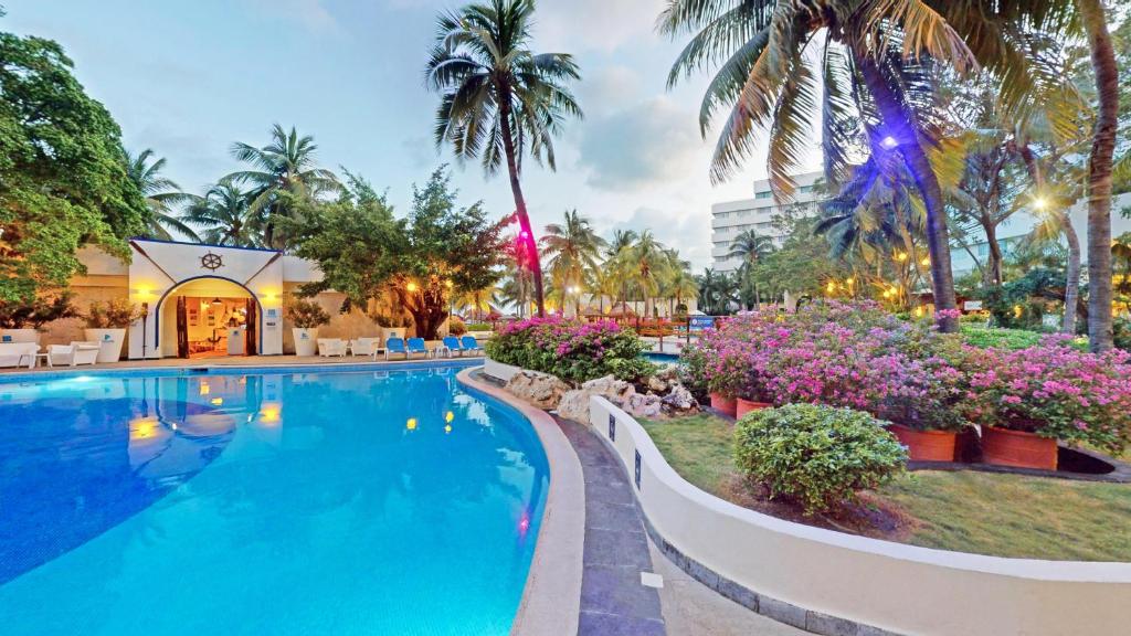 Illuminated pool deck at dusk with purple flowers, palm trees, and loungers.
