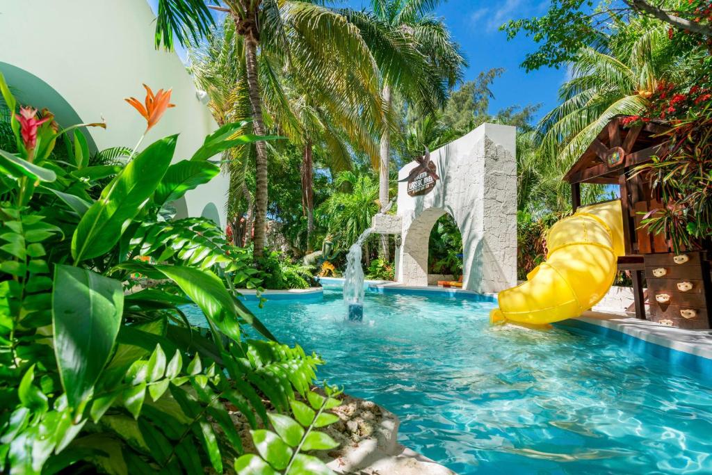 Yellow water slide beside turquoise pool with tropical plants and stone architecture.