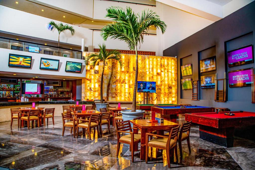 Indoor bar lounge with pool table, tropical plants, wooden tables, and glowing wall art.