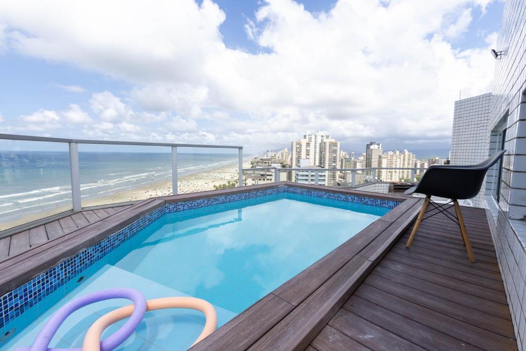 a balcony with a swimming pool and a chair and the beach at Cobertura a beira mar com piscina e churrasqueira in Praia Grande