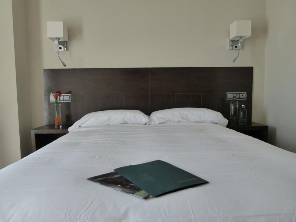 a large white bed with a green book on it at Hotel Río Hortega in Valladolid