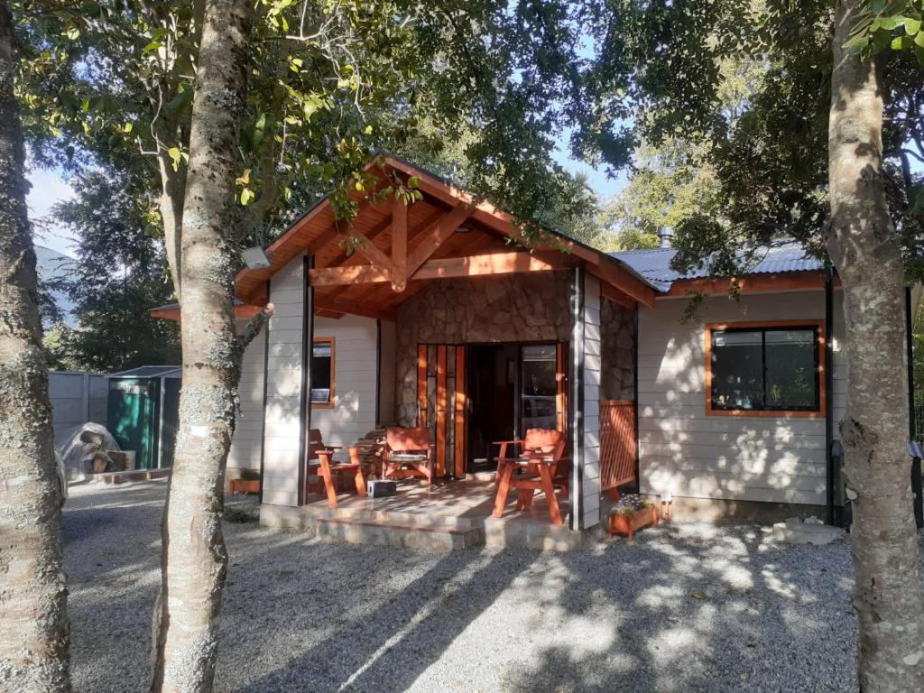 a small white house with chairs and trees at cabañas y tiny house los arrayanes in Pucón