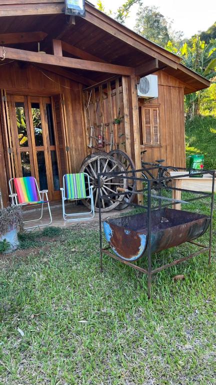 a wooden cabin with two chairs and a boat in the yard at SíTIO DO LILI- uma experiência em meio à natureza in Marques de Sousa