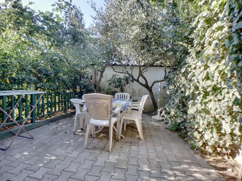 un patio avec des chaises blanches et une table et des arbres dans l'établissement Appartement 6 pers, jardinet privatif, WiFi - FR-1-475-145, à Saintes-Maries-de-la-Mer