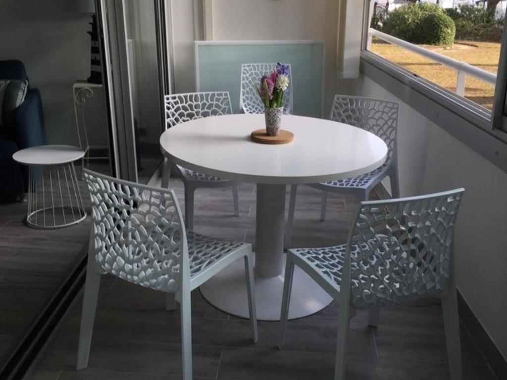 une table blanche et des chaises avec un vase de fleurs dessus dans l'établissement Appartement 2 pièces cabine climatisé pour 4 personnes au Grau du Roi avec parking - FR-1-731-128, au Grau-du-Roi