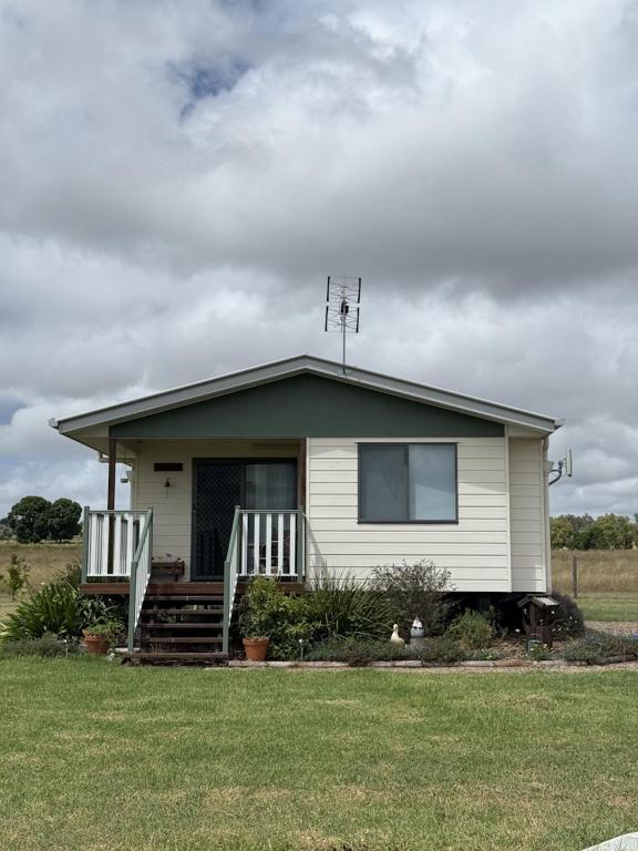 a small white house with a porch and grass at The Cottage in Tingoora