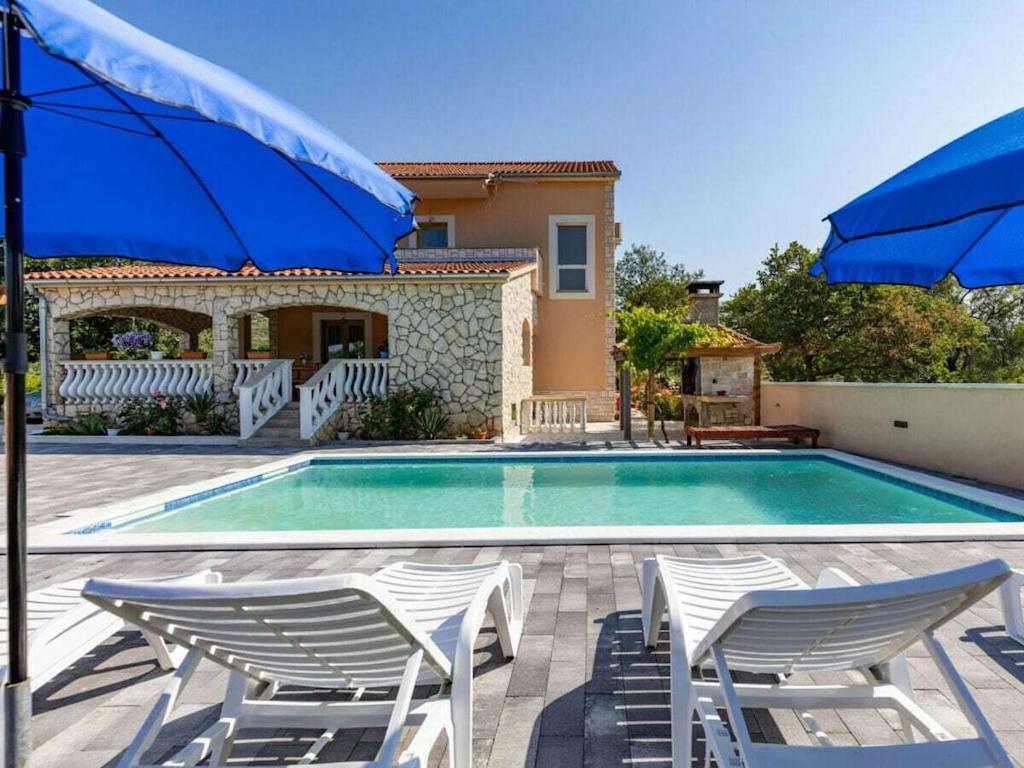 a swimming pool with two chairs and two blue umbrellas at Laetitia with pool Comfortable holiday residence in Banjevci