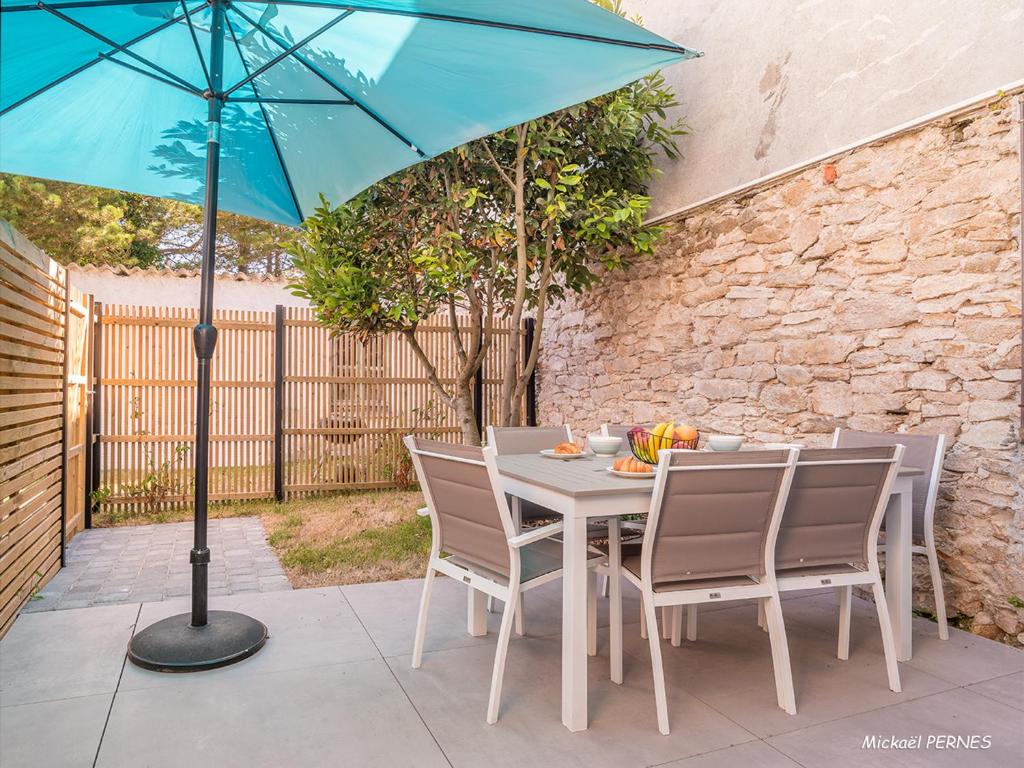 - une table avec des chaises et un parasol bleu sur la terrasse dans l'établissement Maisonette en pierre rénovée avec jardin à 100m de la plage - 5/6 couchages et Wi-Fi - FR-1-349-179, à Larmor-Plage