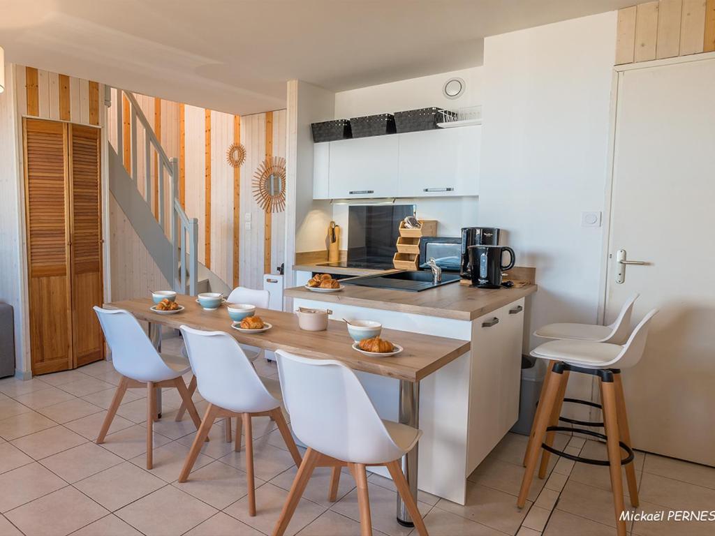une cuisine avec des chaises blanches et une table en bois dans l'établissement Duplex T3 avec 2 parkings à 400m du centre de Lorient - FR-1-349-197, à Lorient