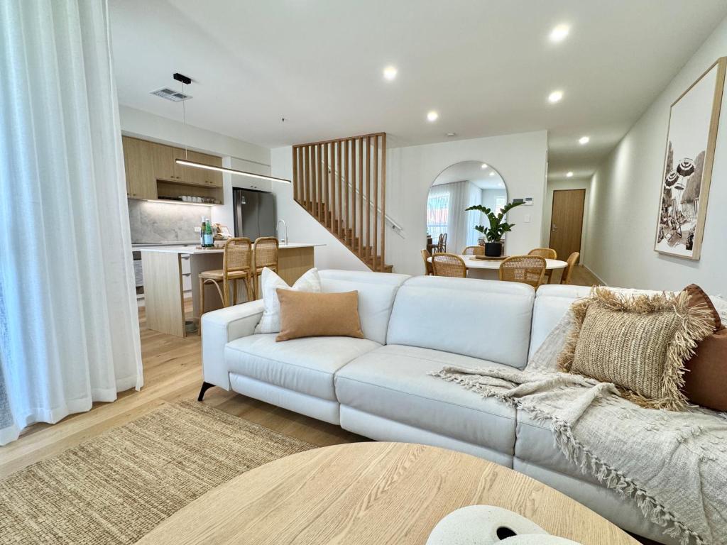 a living room with a white couch and a kitchen at 'Sandbar Escape' 3BR Beach House at Henley Beach in Henley Beach