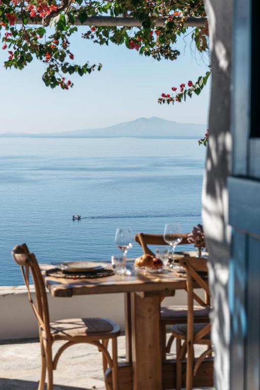 a table with wine glasses and chairs on a patio overlooking the water at Amoni Andros in Agia Eleousa