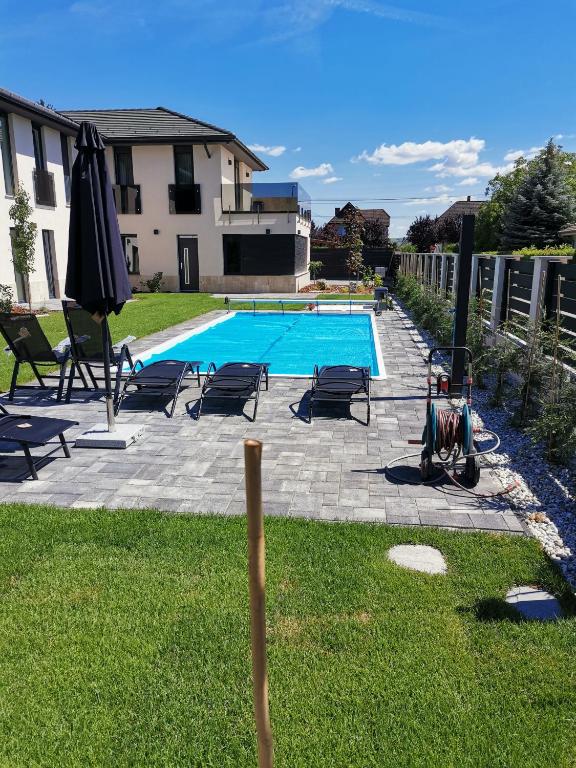 a swimming pool with chairs and an umbrella in a yard at Pipacs 17 by HelloBalatonlelle in Balatonlelle
