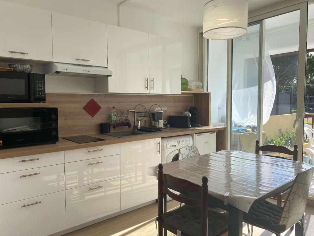 une cuisine avec des armoires blanches et une table avec des chaises dans l'établissement Charmant T1 rénové avec terrasse, climatisation et WiFi à Balaruc-les-Bains - FR-1-553-282, à Balaruc-les-Bains