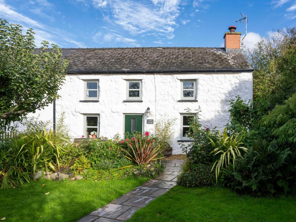 a white house with a green door in a garden at Fern Cottage in Cardigan
