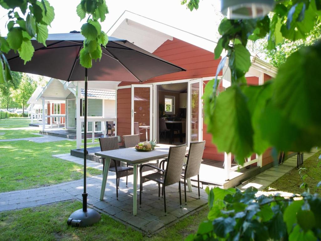 um pátio com uma mesa, cadeiras e um guarda-sol em Lodge in Brabant with Cozy Covered Terrace em Oirschot