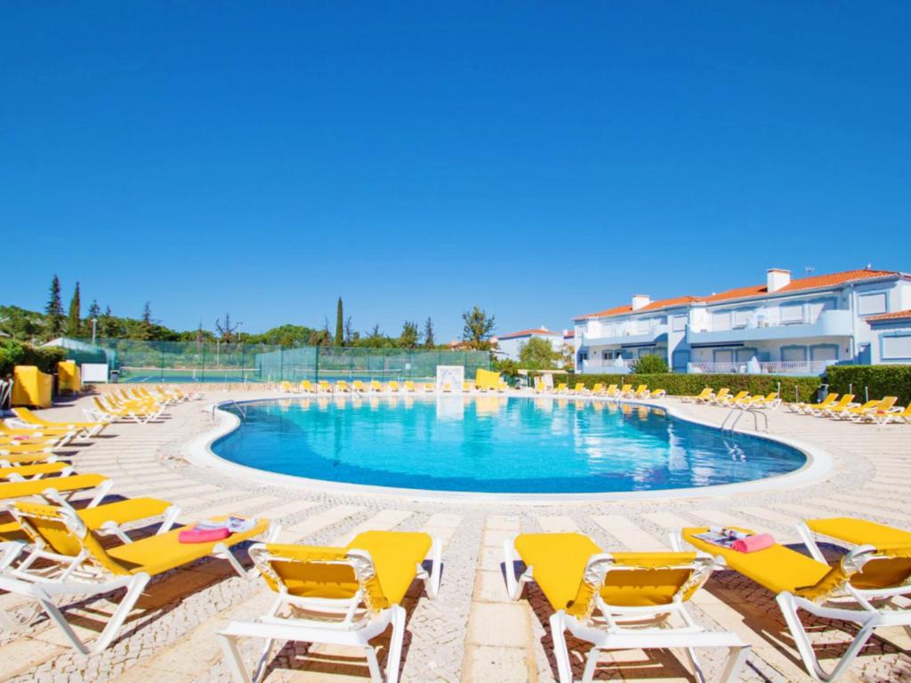 a swimming pool with yellow lounge chairs and a beach at Apartamento Oásis Parque 1 in Portimão
