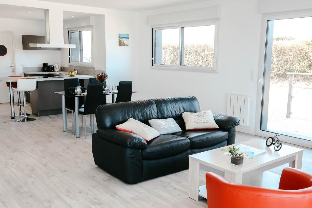 Il comprend un salon avec un canapé en cuir noir et une cuisine. dans l'établissement 500m de la mer, maison moderne avec jardin pour 4, à Brignogan-Plage