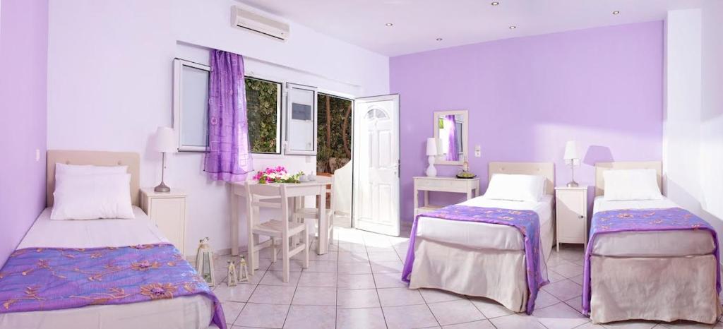 a purple and white room with two beds and a table at Primavera Beach Hotel Studios & Apartments in Malia