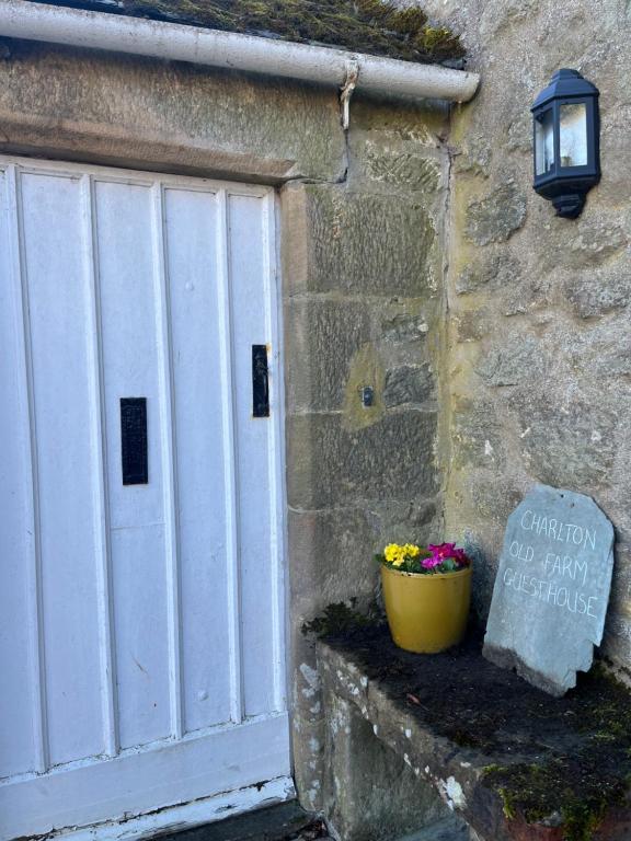 a building with a white door and a pot of flowers at Charlton Old Farm Guesthouse in Greenhaugh