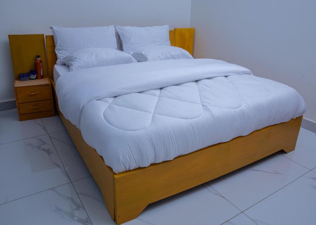 a bed with a wooden frame with white sheets and pillows at Holly apartment in Kigali