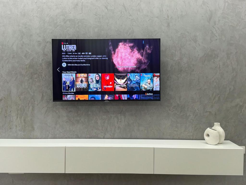 a tv hanging on a wall above a white dresser at Elysian Escape Apartment in Sarandë