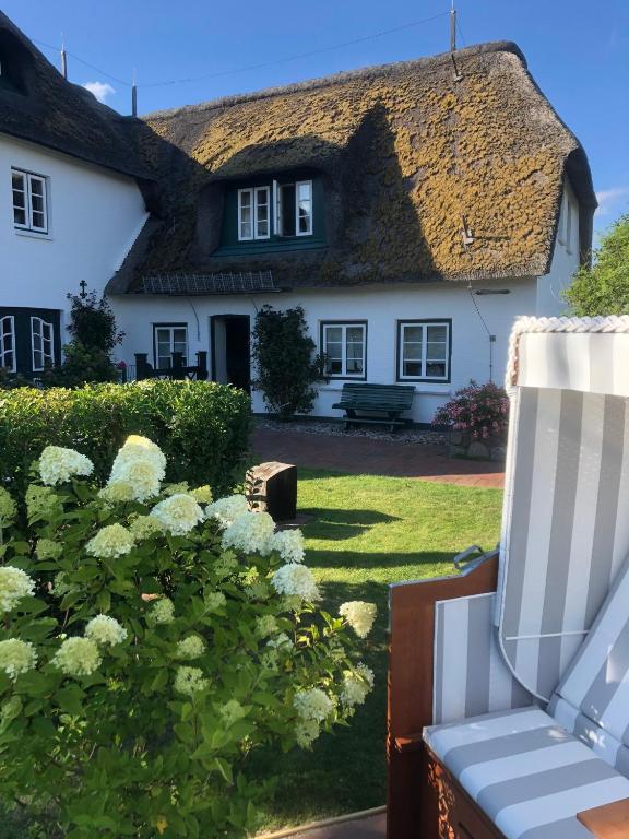 a white house with a thatched roof and a chair at Deichhof Whg Luana in Dunsum