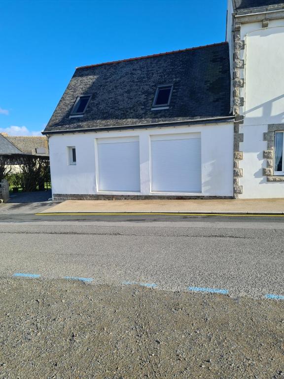 une maison blanche avec deux portes de garage dans une rue dans l'établissement maison face à la mer, à Trégunc