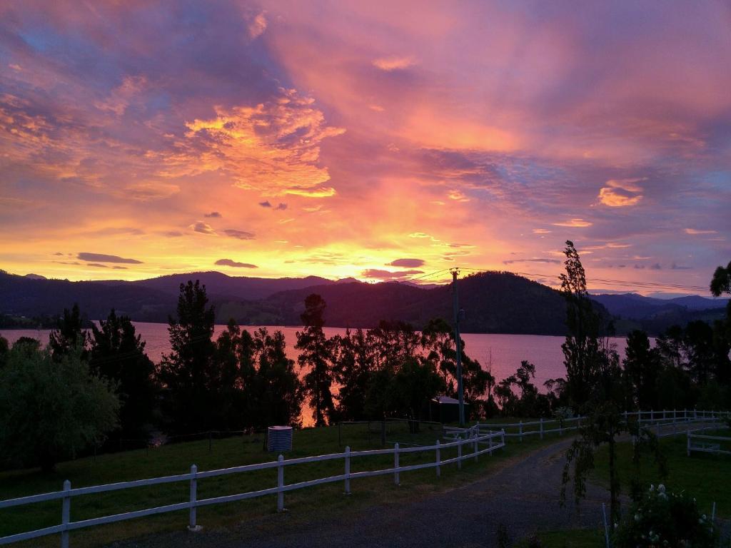 a sunset over a body of water with a fence at Ambience on Huon Bed & Breakfast in Cygnet