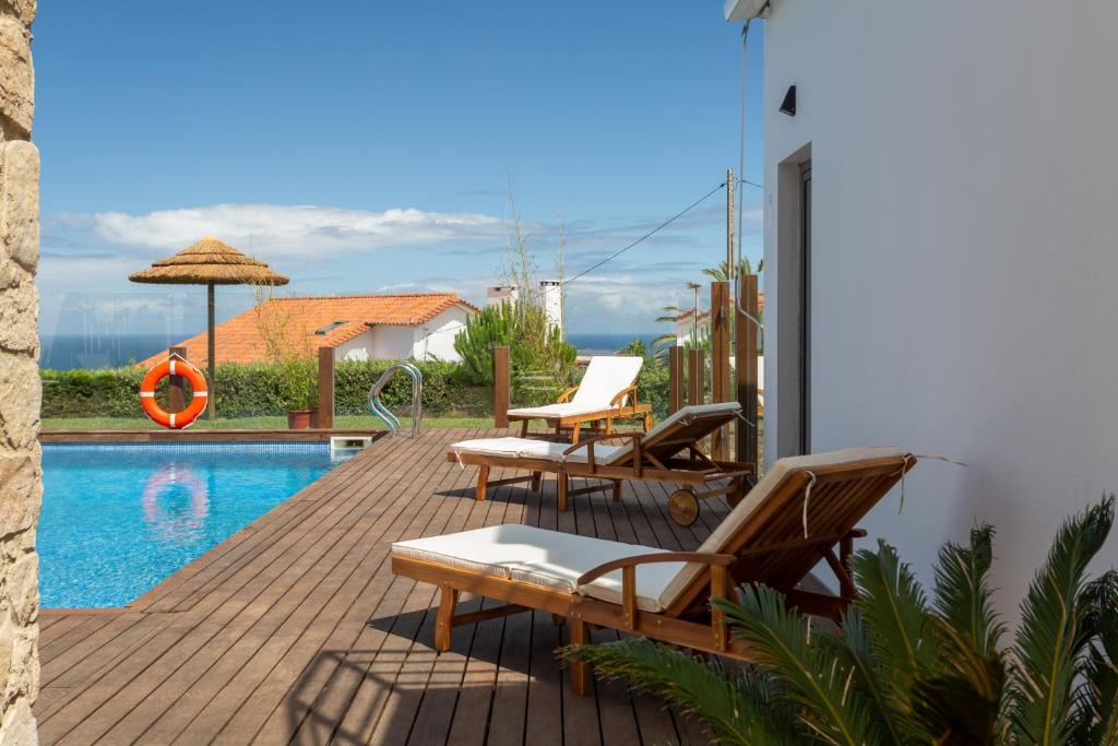 a wooden deck with chairs and a swimming pool at Penedo Escape Sea Suites in Colares