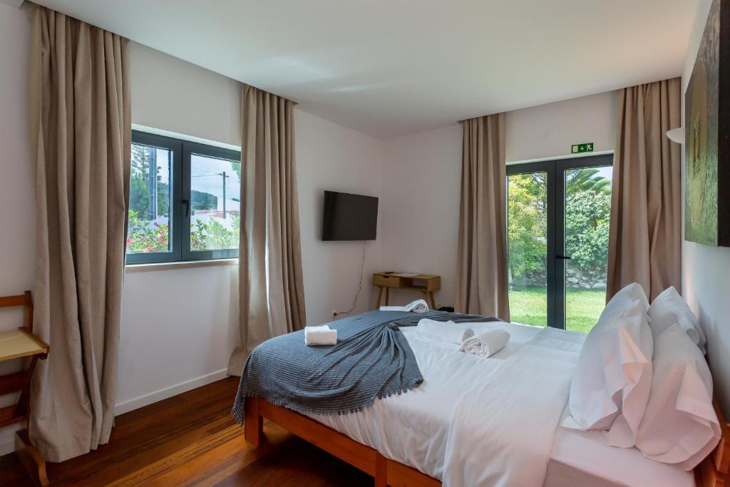 a bedroom with a bed with white sheets and windows at Penedo Escape Sea Suites in Colares
