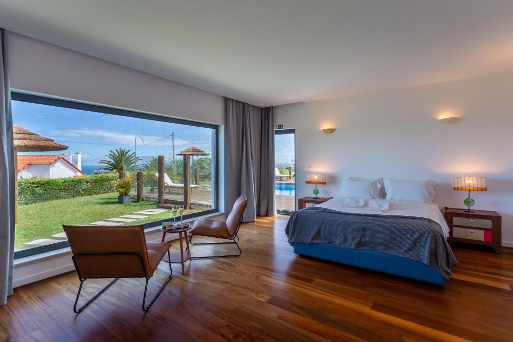 a bedroom with a bed and a large window at Penedo Escape Sea Suites in Colares