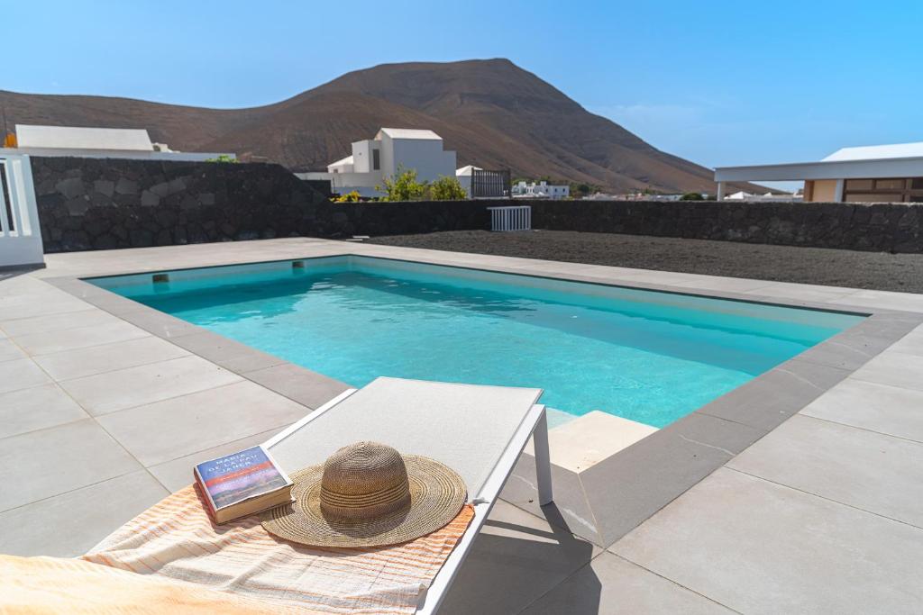 a hat and a book sitting on a bench next to a swimming pool at Vv Villa Secretos de Yaiza 2 by HH - private pool in Yaiza