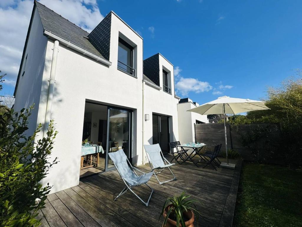 a white house with a deck with chairs and an umbrella at Ty Kerbihan, confortable maison au calme, 200m plage in La Trinité-sur-Mer