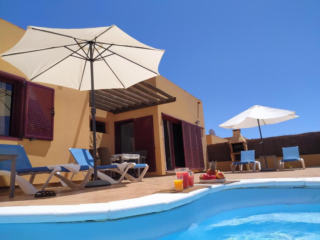 a house with a swimming pool with chairs and an umbrella at Villa Dunas Fuerteventura in Lajares