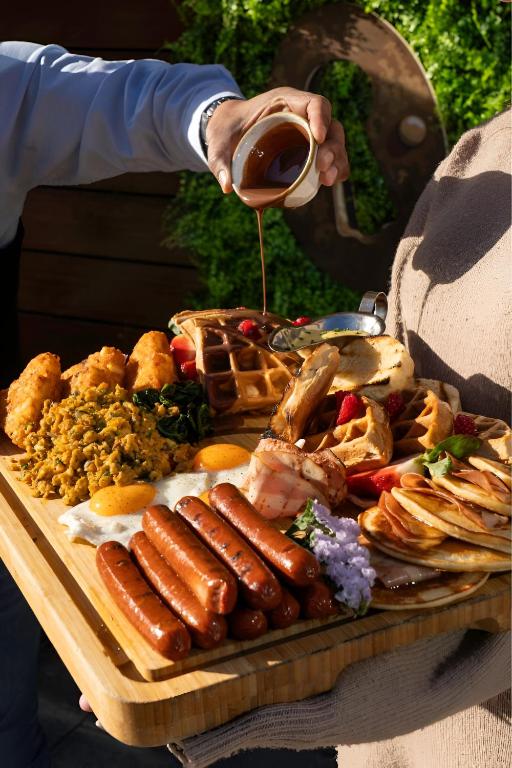 a person holding a bottle of wine over a tray of food at La Petite Résidence- Private in Kigali