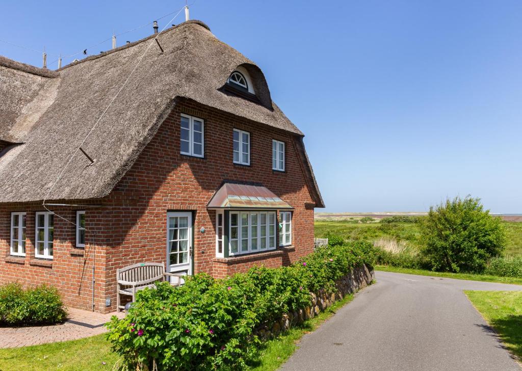 ein Backsteinhaus mit einem Strohdach auf einer Straße in der Unterkunft Ferienwohnung Lachmöwe in Norddorf