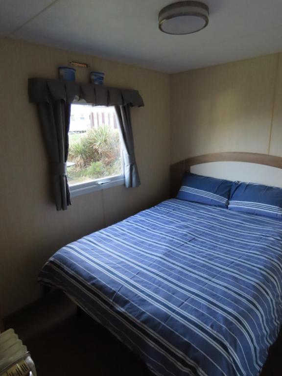 a bedroom with a bed with a blue comforter and a window at 3 bedroom static caravan with sea view in Clarach Bay Holiday Village Abi horizon in Aberystwyth