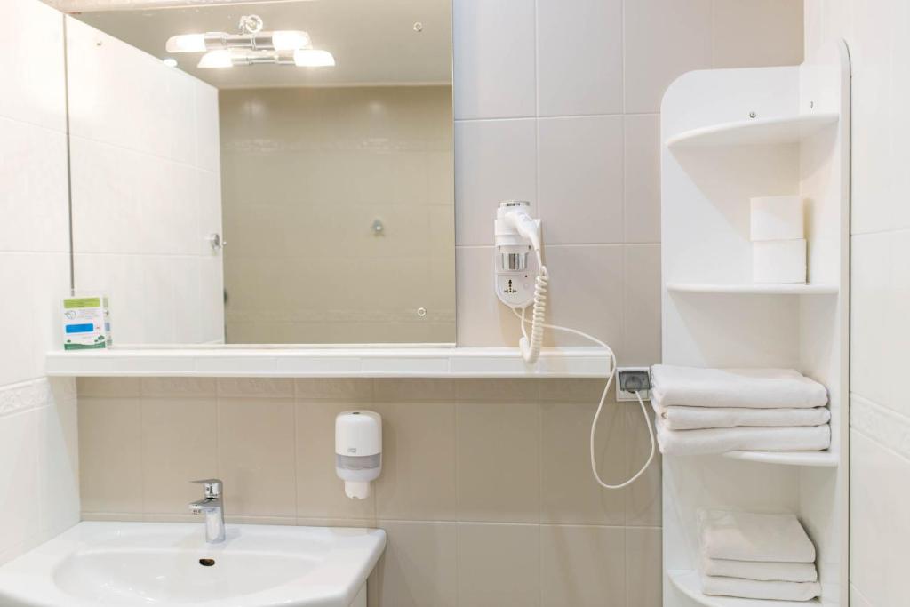 Compact neutral-toned bathroom sink with mirror, wall-mounted hairdryer, soap dispenser, and stacked white towels on shelving