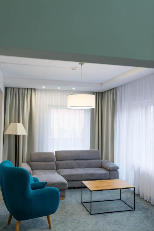 Bright lounge area with grey sofa, teal accent chair, pendant light and sheer curtains.