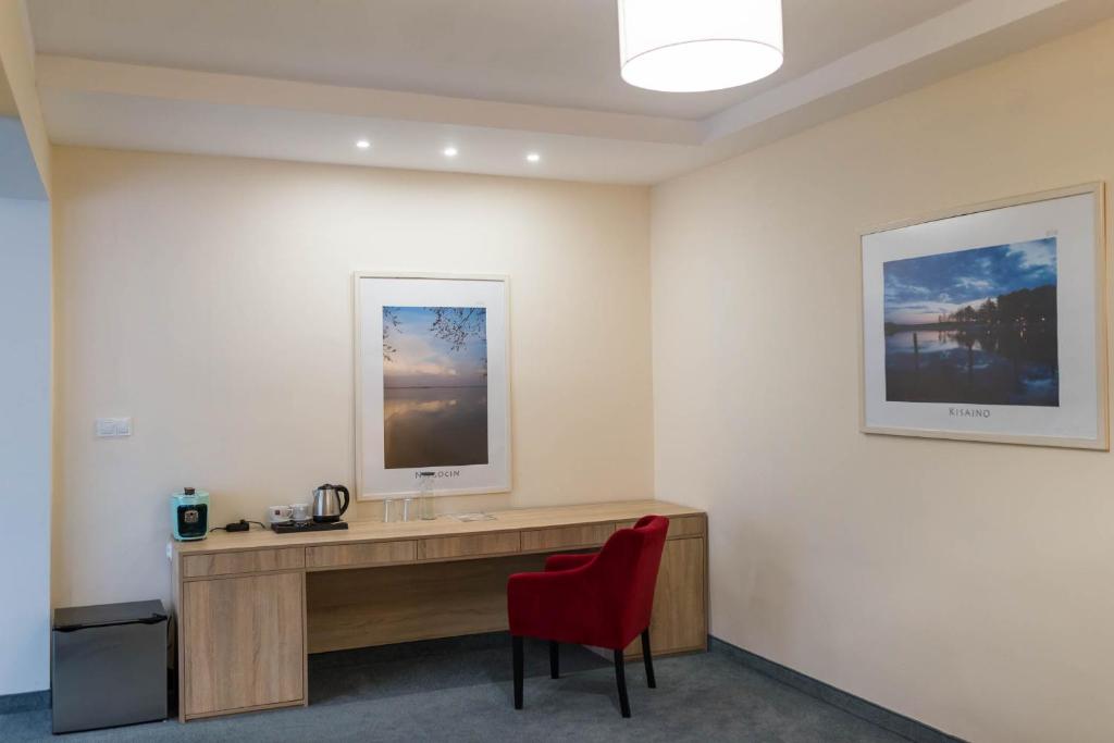 Guest room workspace with wooden desk, kettle, red upholstered chair, framed wall art.