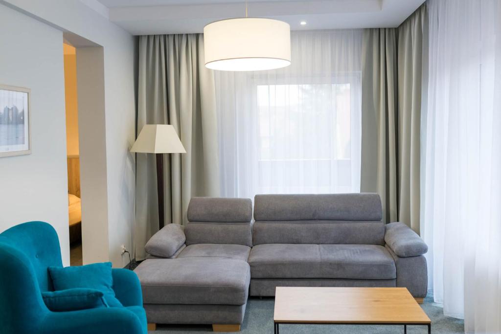 Modern hotel living room with grey sectional sofa, teal armchair, wooden coffee table, soft light.