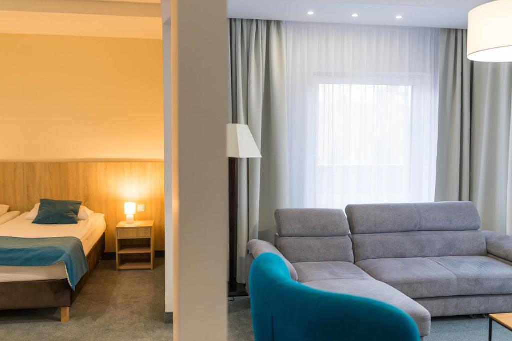 Suite showing bedroom and living area divided by partial wall, grey sofa and blue chair.