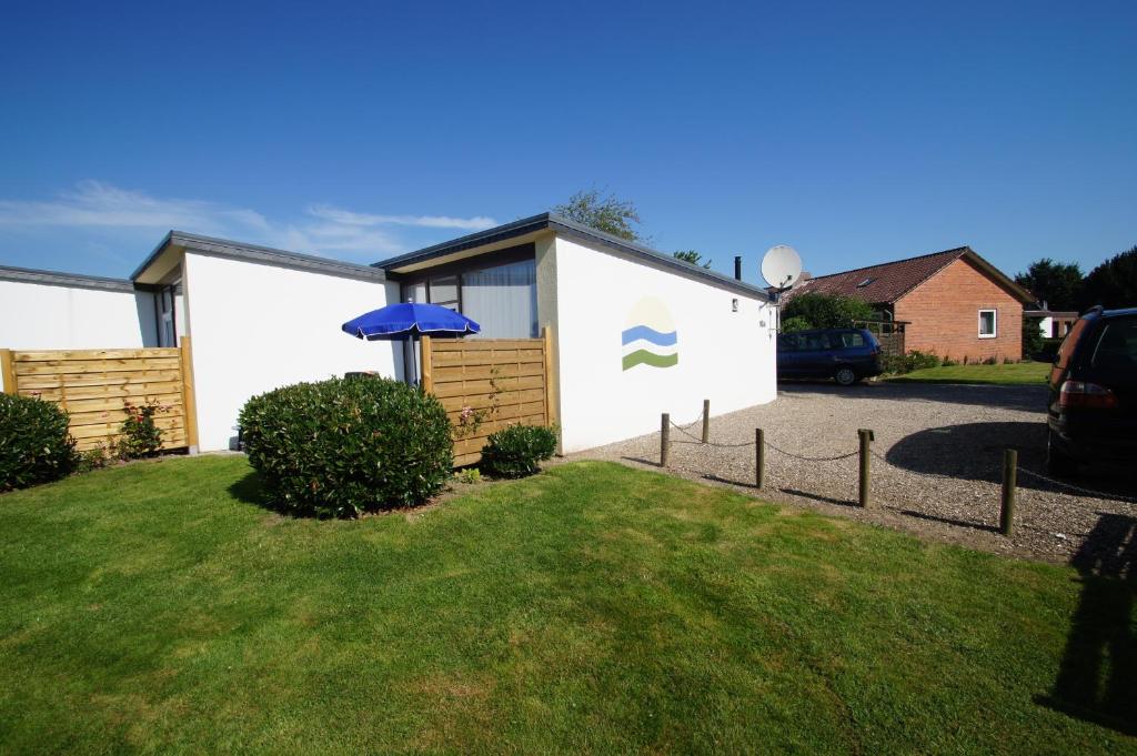 un edificio blanco con una sombrilla azul junto a un patio en Ferienbungalow 5, en Dahme
