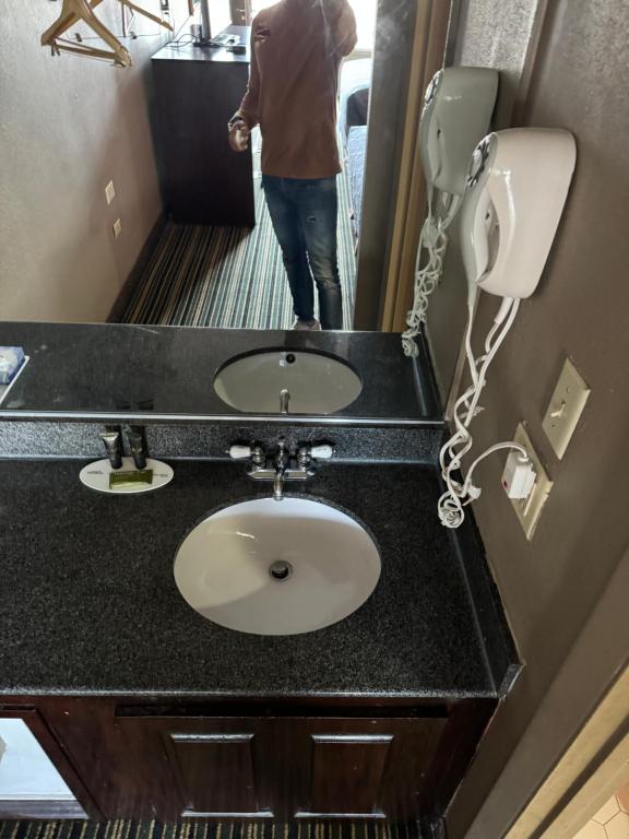 eine Person, die vor einem Waschbecken in einem Badezimmer steht in der Unterkunft labh inc Motel in Norfolk