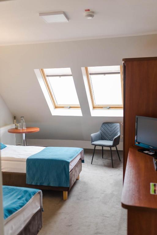 Attic guest room with two beds, skylight windows, grey armchair, wooden TV cabinet.