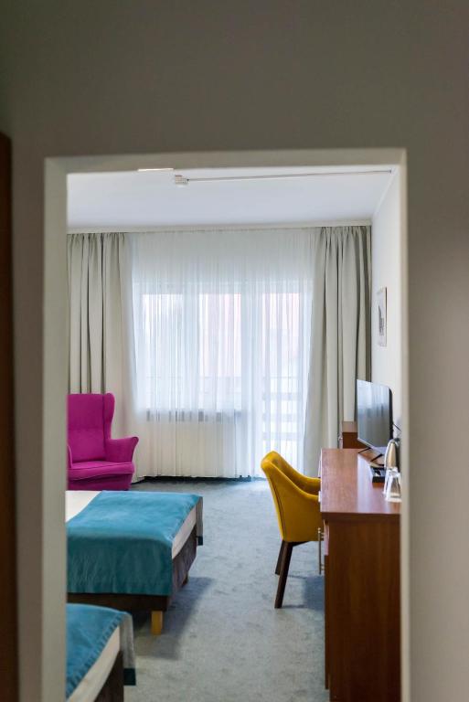 View through doorway into bright guestroom with twin beds, pink armchair, yellow desk chair.