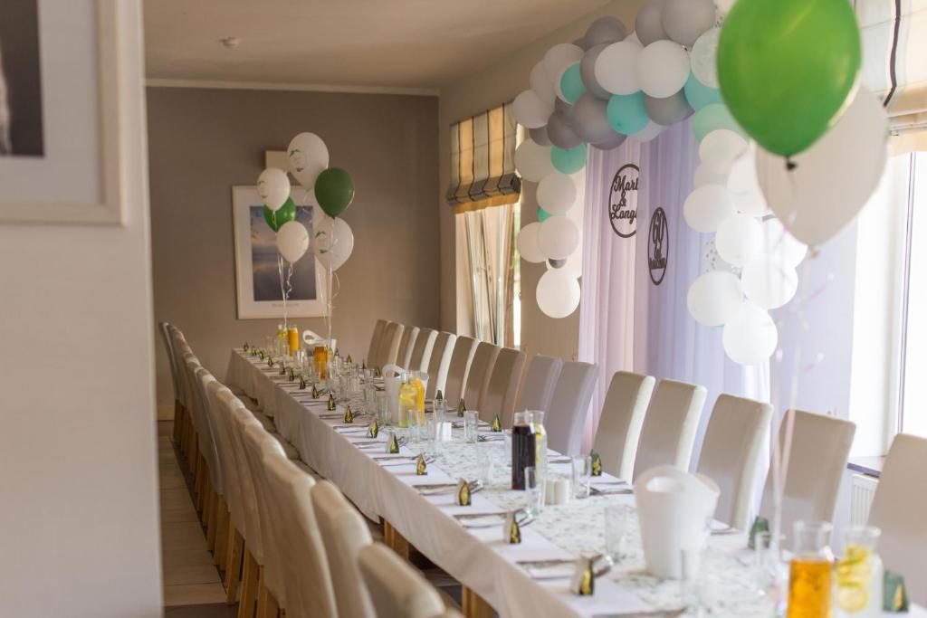 Long banquet table set for celebration with white chairs, balloon arch and table decorations.