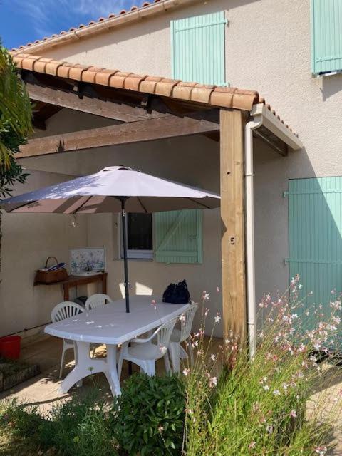 - une table et des chaises avec un parasol en face d'une maison dans l'établissement résidence les marines, à Saint-Vincent-sur-Jard