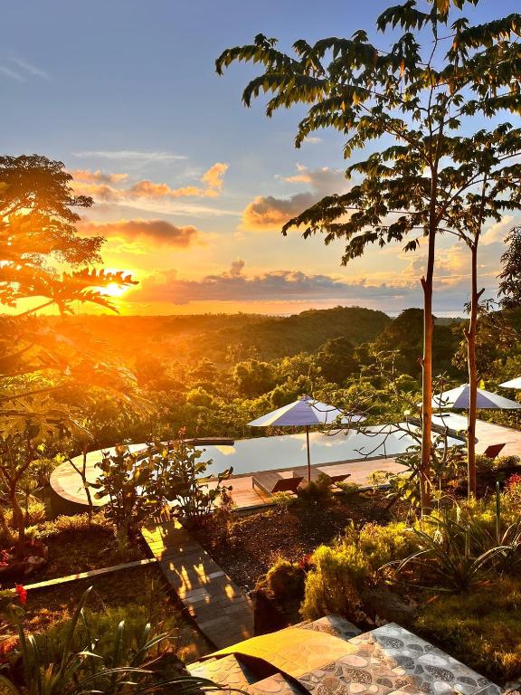 a sunset over a lake with umbrellas and a pool at Kubuhill Sunset Bungalow in Nusa Penida