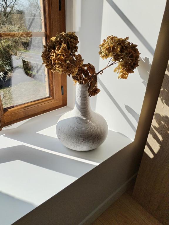 un vase blanc avec des fleurs assis sur un rebord de fenêtre dans l'établissement Au plaisir de l'ivoie chambre double, à Le May-sur-Èvre
